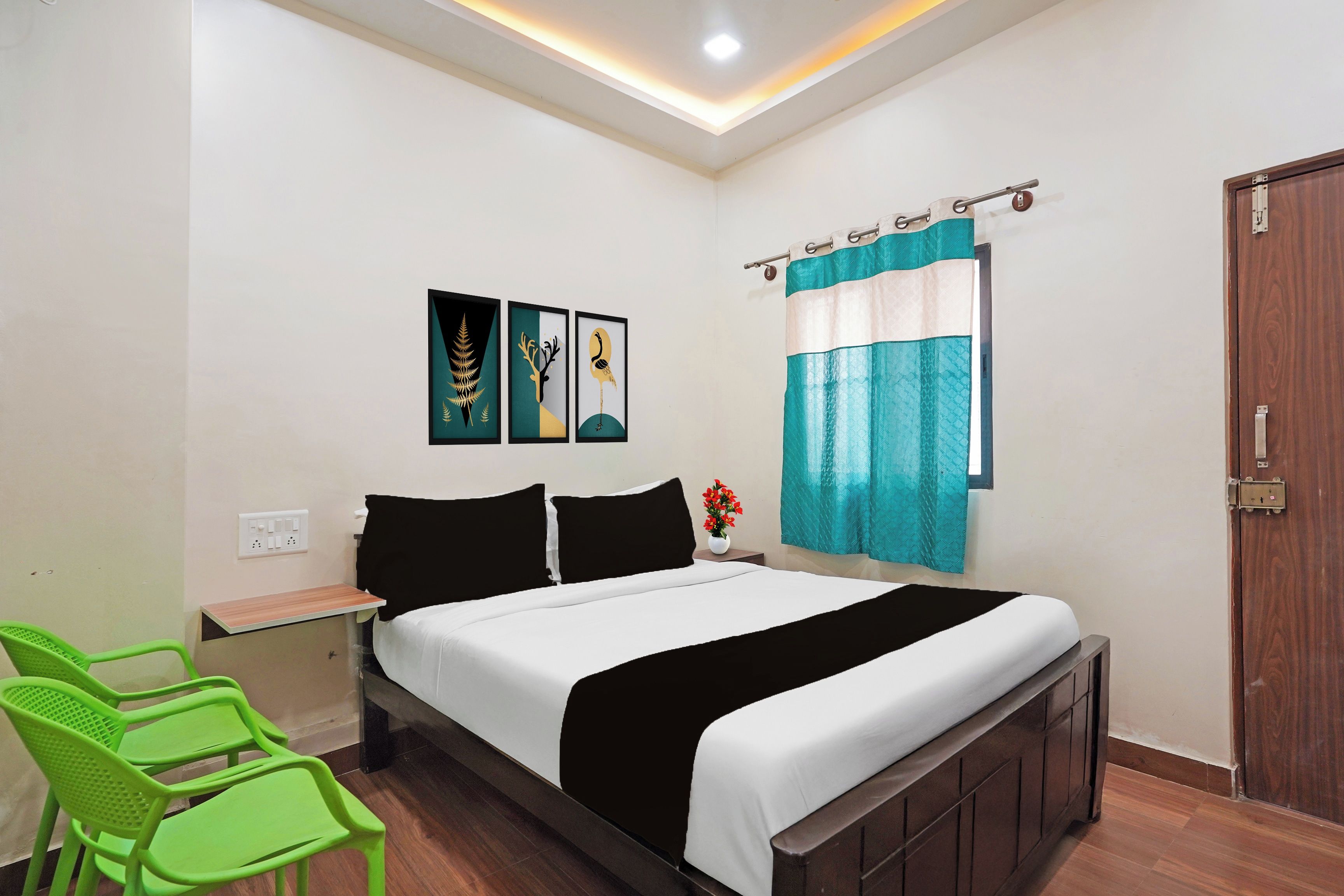 Une chambre d’hôtel avec un lit, des chaises vertes, une table de chevet, une étagère fixée au mur et une porte.