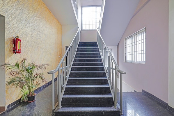 Una escalera con barandillas metálicas que conduce a un piso superior, un extintor de incendios en la pared y una planta en maceta a la izquierda.
