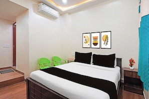 Una habitación de hotel con una cama, una mesita de noche, una silla verde, una pequeña mesa y un aire acondicionado instalado en la pared.