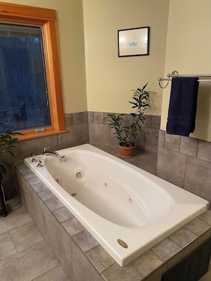 A bathroom with a freestanding bathtub, a potted plant, a towel rack, and a framed picture on the wall.