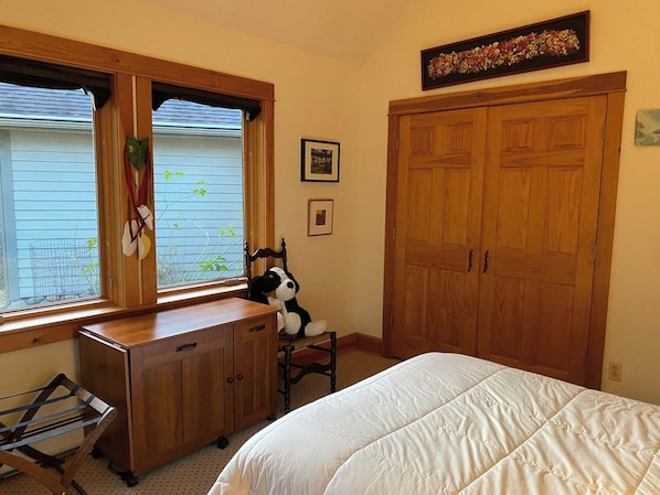 A bedroom with a bed, a wooden dresser, a window with blinds, a door, and a wall-mounted picture.