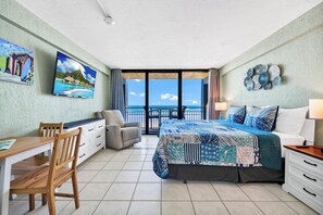 Ein Schlafzimmer mit einem Bett, einem Schreibtisch, einem Sessel, einem Fernseher und Meerblick.
