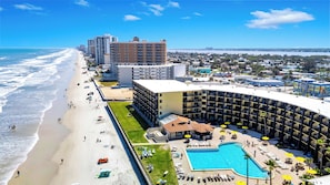 Een hotel aan het strand met een zwembad, toegang tot het strand en hoge gebouwen op de achtergrond.