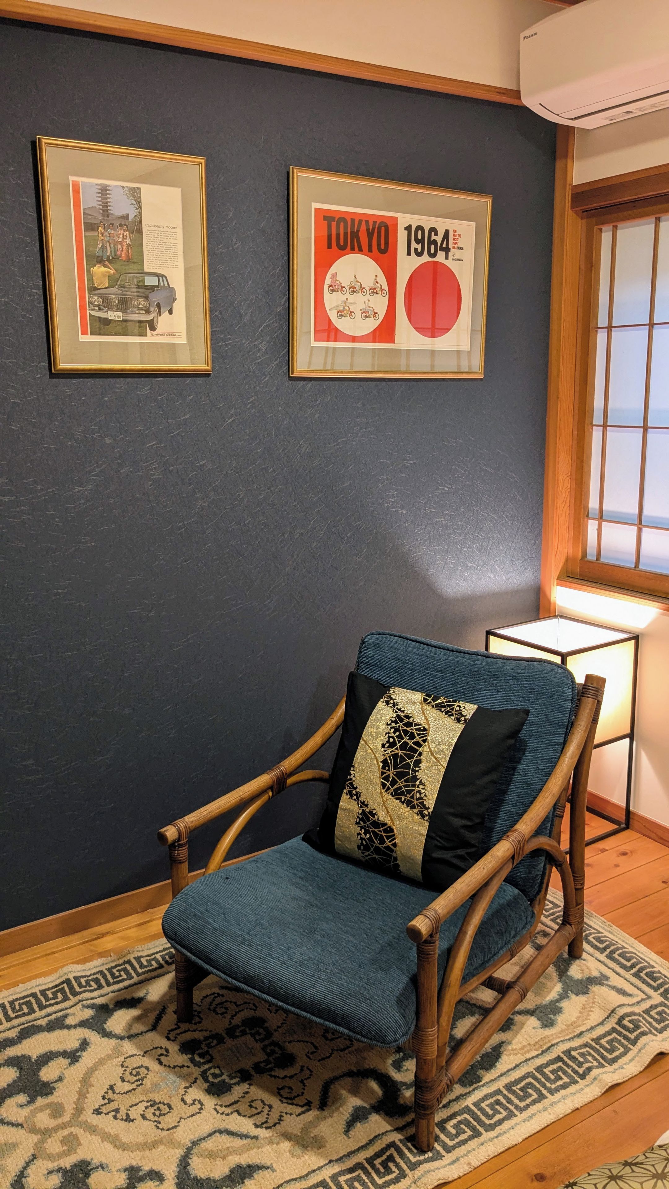 A room with a wooden rocking chair, a framed picture of a car, and a framed Tokyo 1964 poster.
