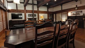 A dining area with a long wooden table and chairs, a television, and a clock on the wall. - 1880s Kominka - Luxury Renovation - 5 mins from Goryu - Rental Van Available (Hakuba)