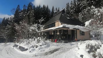 Un edificio di due piani con un portico coperto, circondato da alberi innevati e un cielo sereno.