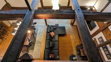 Un interior moderno con vigas de madera a la vista, un sofá de cuero negro y una zona de comedor con sillas metálicas y lámparas colgantes.