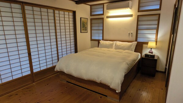 A traditional Japanese-style bedroom with a wooden floor, a bed with white bedding, sliding shoji doors, and a bedside table with a lamp. - 1880s Kominka - Luxury Renovation - 5 mins from Goryu - Rental Van Available (Hakuba)