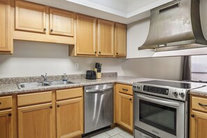 A kitchen with wooden cabinets, a stainless steel dishwasher, a built-in oven, and a range hood.