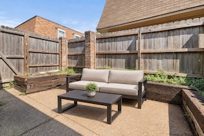 An outdoor patio with a sofa and a table, surrounded by a wooden fence and a brick wall.