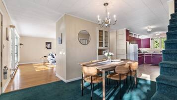 A spacious living area with a dining table, chairs, a chandelier, and a view of the kitchen.