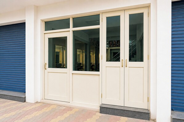 A set of white double doors with glass panels, a blue shutter door to the left, and a tiled walkway leading to the entrance.