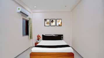 A hotel room with a bed, a nightstand, a window with curtains, an air conditioning unit, and three wall-mounted artworks.