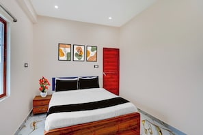 A bedroom with a bed, a nightstand, a vase with flowers, and three framed artworks on the wall. - OYO 840189 Vijay Shree Marriage Hall (Gopalganj)