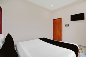 A hotel room with a bed, a wooden door, and a flat-screen TV mounted on the wall.