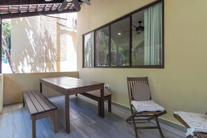 Une terrasse couverte avec une table et des chaises, une fenêtre avec des rideaux et un ventilateur de plafond.