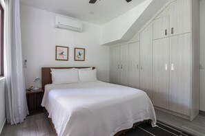 Une chambre à coucher comprenant un lit, une table de chevet, des lampes de chevet, des œuvres d’art encadrées, un appareil de climatisation et une armoire.