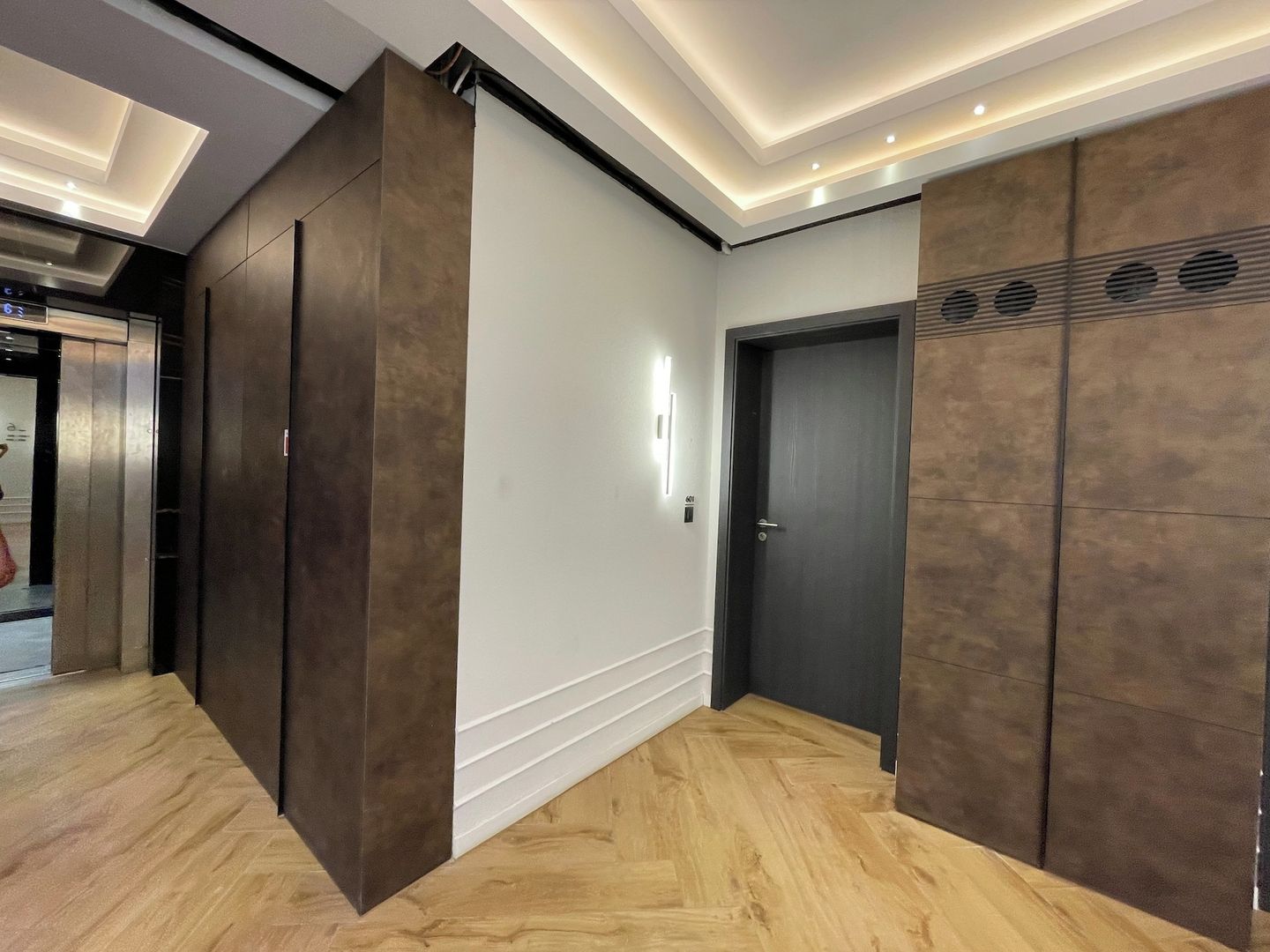 Ein Flur mit Holzboden, einer dunklen Tür und einer Wand mit einer eingelassenen Vertiefung.