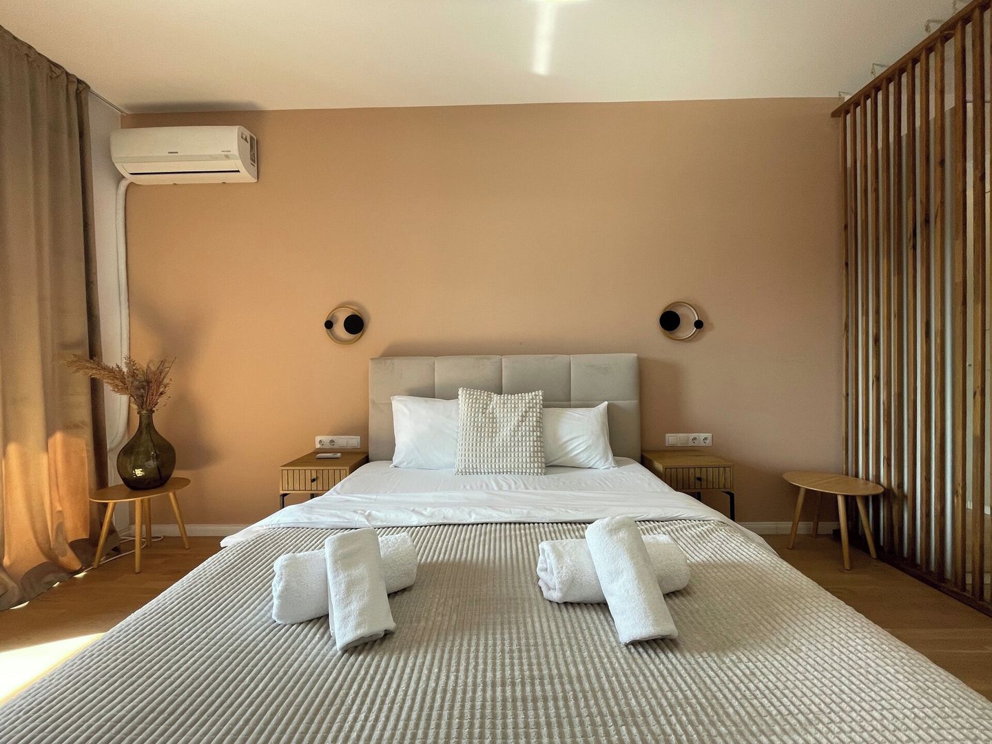 Ein Hotelzimmer mit einem Bett, Nachttischen, einer Vase mit Trockenpflanzen und einer Klimaanlage.