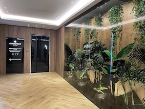A modern hotel lobby with a wooden floor, a glass wall with plants, and a sign for the Cosmopolitan Office. - Golden Berryl w AC and Smart TV (Brașov)