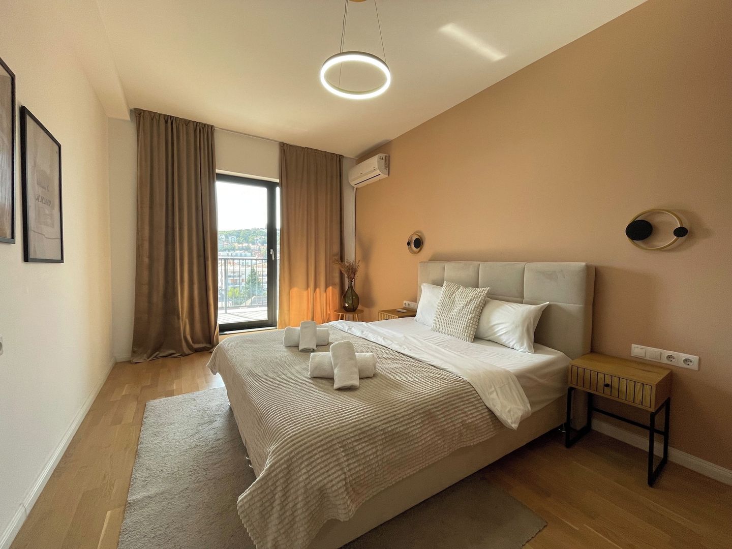 Ein modernes Schlafzimmer mit einem großen Bett, einem Nachttisch, einer Wandleuchte und einem Fenster mit Vorhängen.