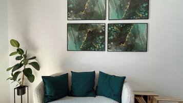 Una habitación con un sofá blanco con textura, cojines verde azulado y una planta en un soporte negro.