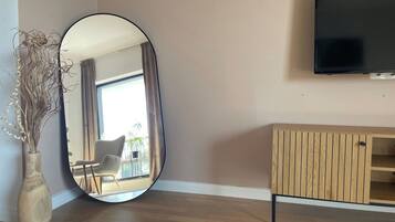 A room with a large oval mirror, a wooden cabinet, and a flat-screen TV mounted on the wall.
