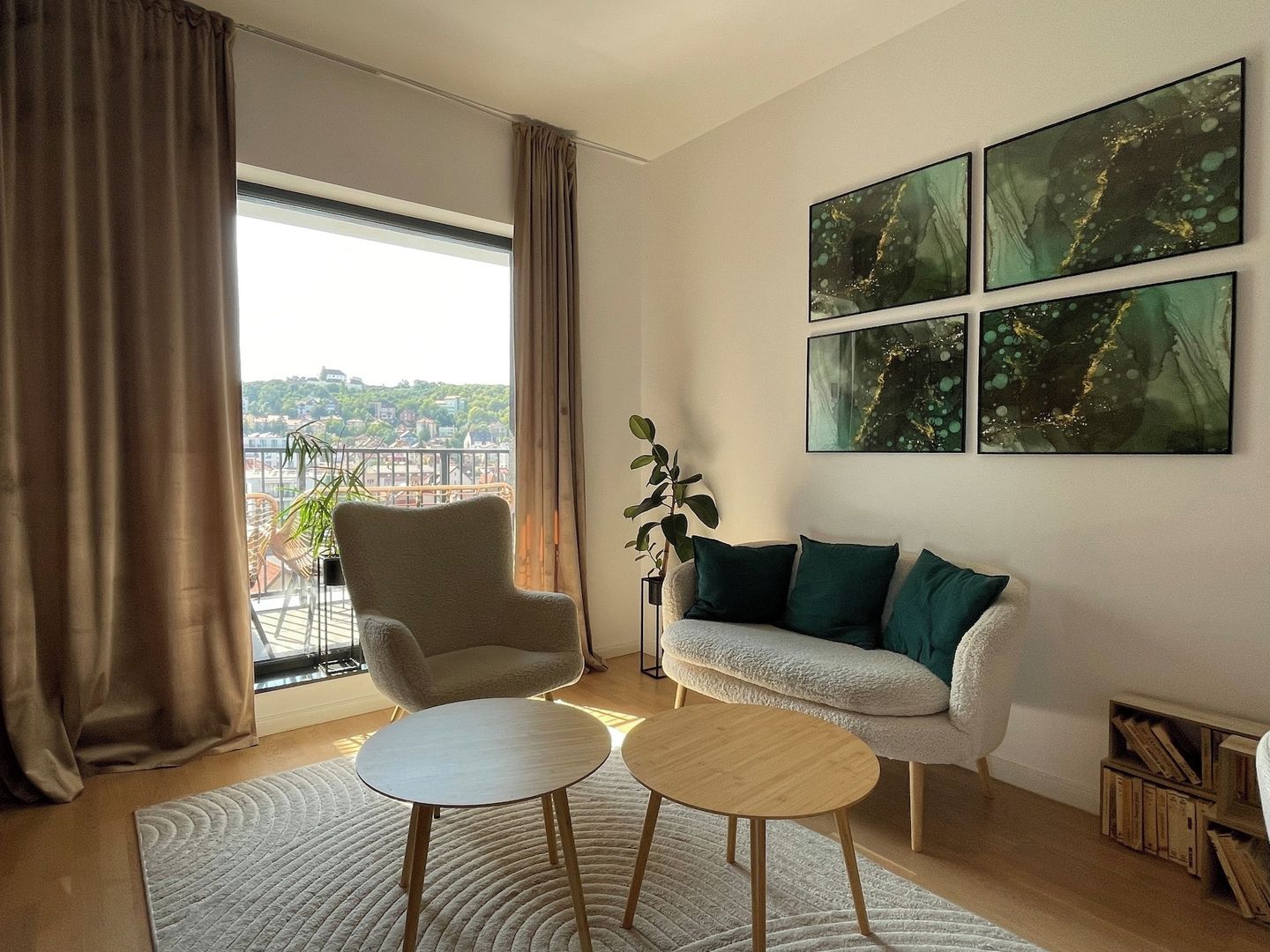 Ein modernes Wohnzimmer mit einer Couch, einem Sessel und zwei kleinen Tischen. An den Wänden befinden sich abstrakte Gemälde und durch große Fenster ist ein Blick auf die Stadt möglich.