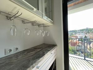 A kitchen with a marble countertop, wine glasses hanging on a rack, and a balcony with a view of buildings. - Golden Berryl w AC and Smart TV (Brașov)