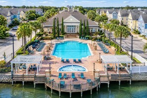 A resort with a central swimming pool, lounge areas, and a dock extending into a body of water. - Storybook House | 4BR Disney Area Retreat (Kissimmee)