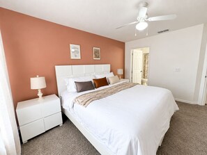 A bedroom with a bed, nightstands, a ceiling fan, and a door leading to another room. - Storybook House | 4BR Disney Area Retreat (Kissimmee)