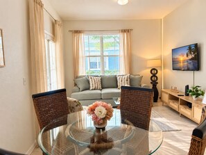 A living room with a glass table, two wicker chairs, a sofa, and a TV on the wall. - Storybook House | 4BR Disney Area Retreat (Kissimmee)
