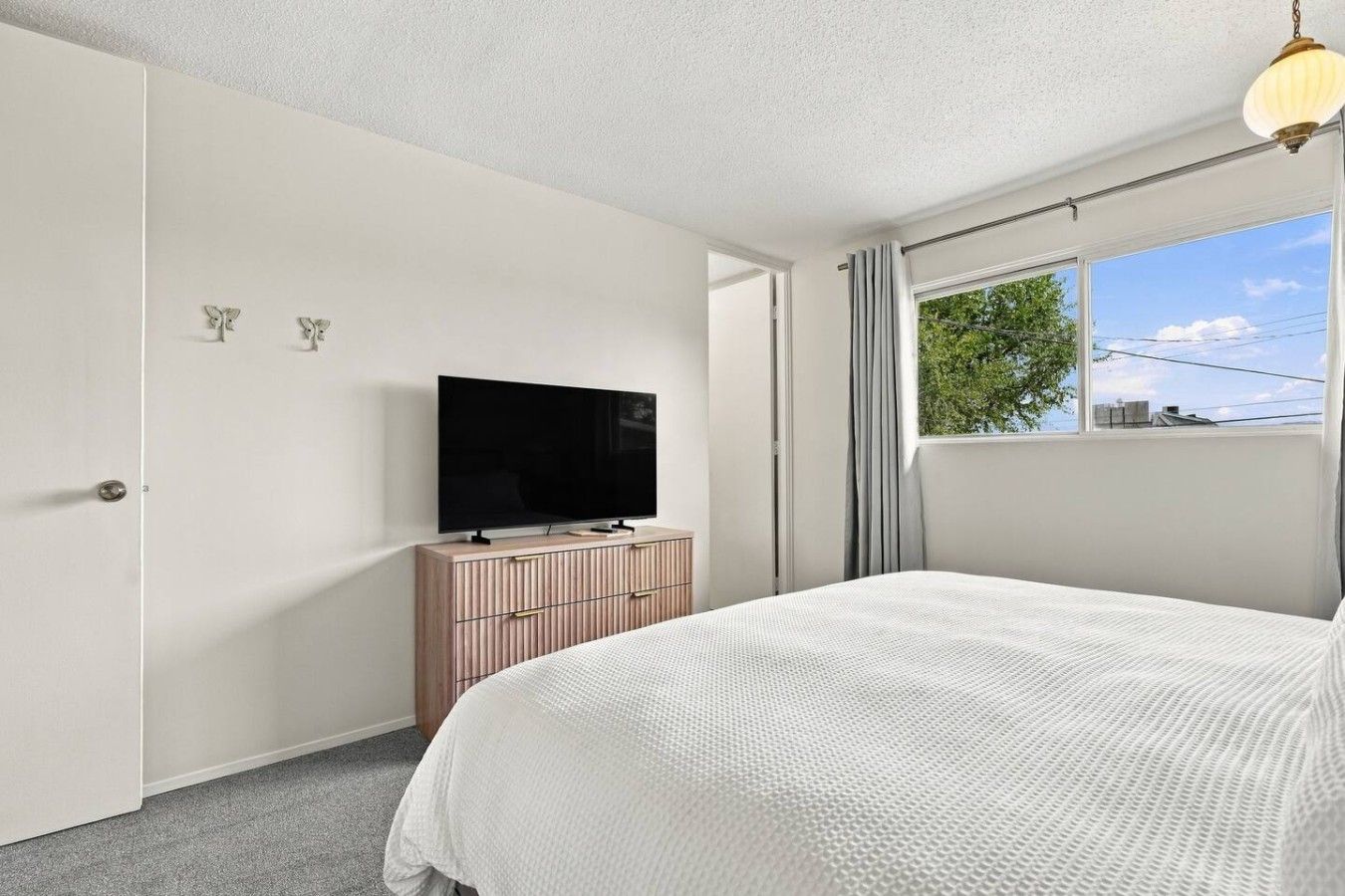 A bedroom with a bed, a television on a wooden dresser, and a window with curtains.