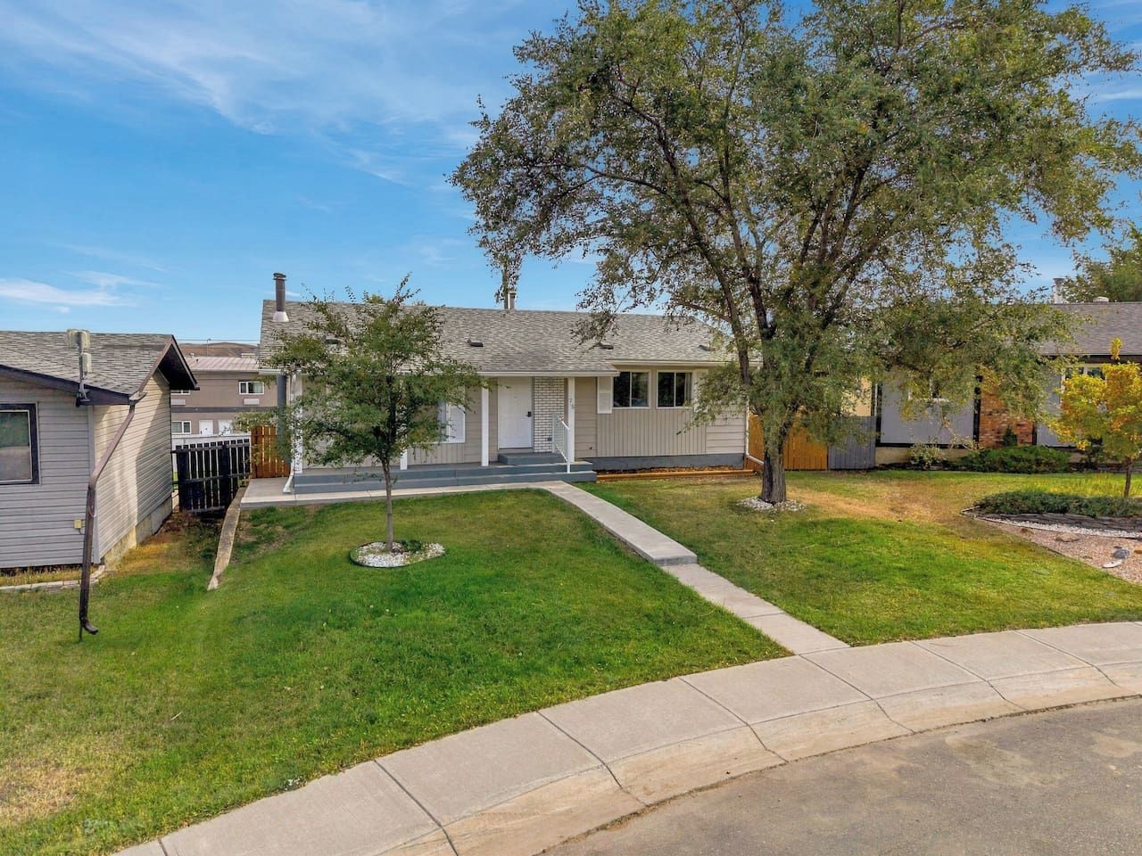 A residential area with a house featuring a front porch, a small lawn, and a tree.