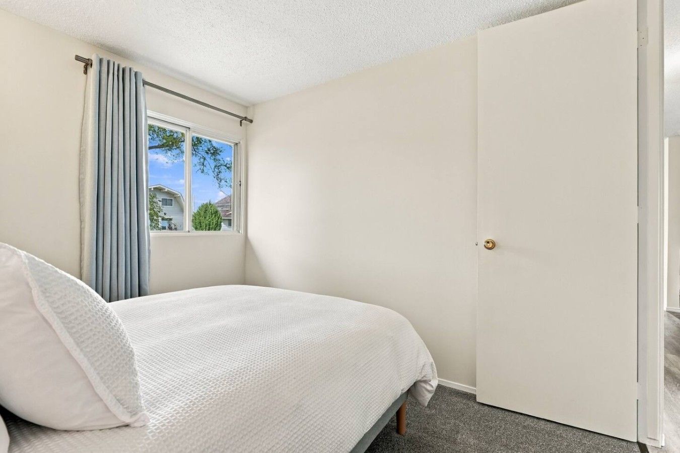A bedroom with a bed, a window with curtains, and a door.