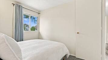A bedroom with a bed, a window with curtains, and a door.