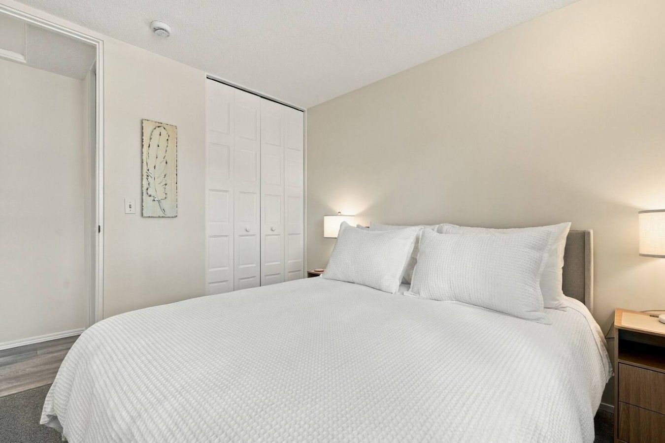 A bedroom with a large bed, a wardrobe, and a wall-mounted artwork.