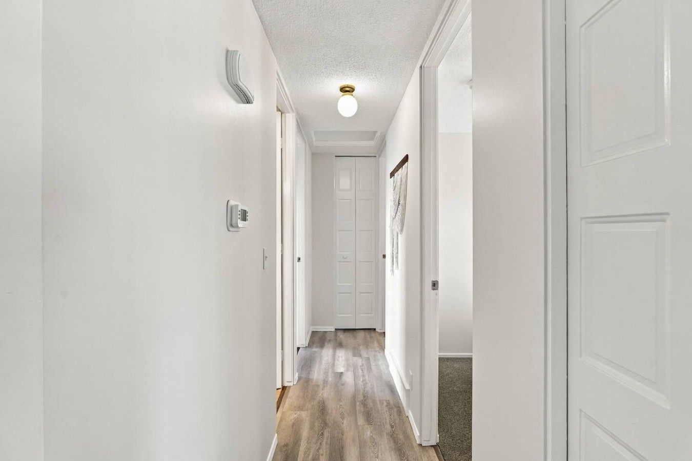 Un couloir aux murs blancs, doté d’un plancher en bois et d’un luminaire au plafond.