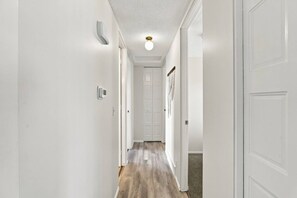 A hallway with white walls, a wooden floor, and a ceiling light.