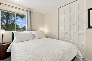 Ein Schlafzimmer mit einem Bett, einem Nachttisch, einem Fenster mit Vorhängen und einer Tür.