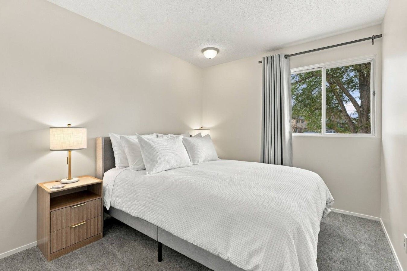 Une chambre à coucher avec un lit, des tables de chevet, une lampe et une fenêtre avec des rideaux.