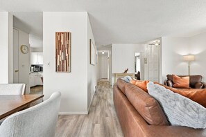 Ein modernes Wohnzimmer mit einer braunen Ledersofa, einem Esstisch mit Stühlen und einer Küche im Hintergrund.