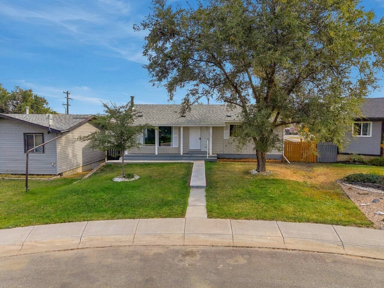 A residential house with a front yard, a driveway, and a small tree.