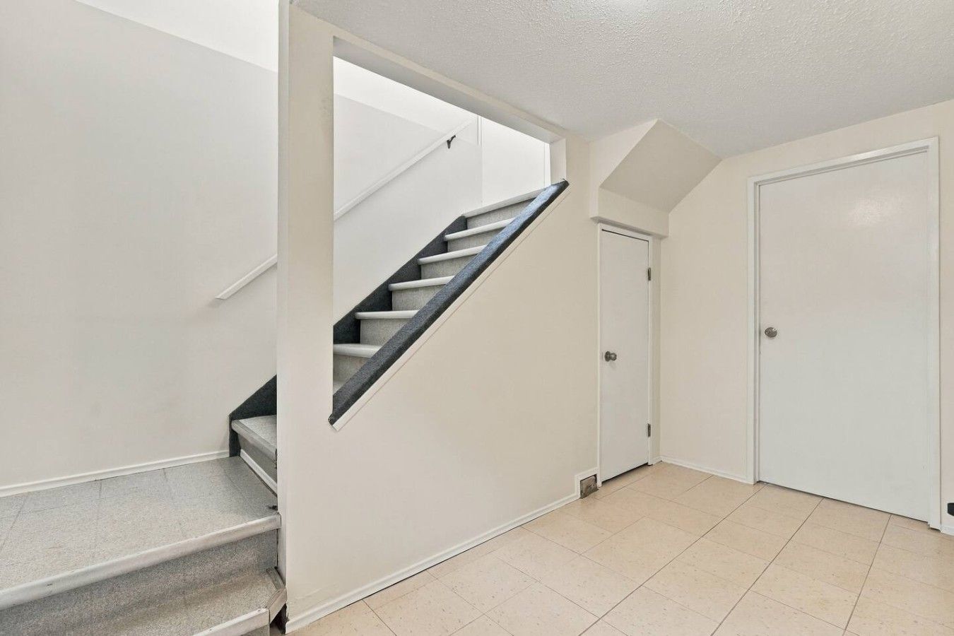 A staircase leading to a door, a tiled floor, and a plain white wall.