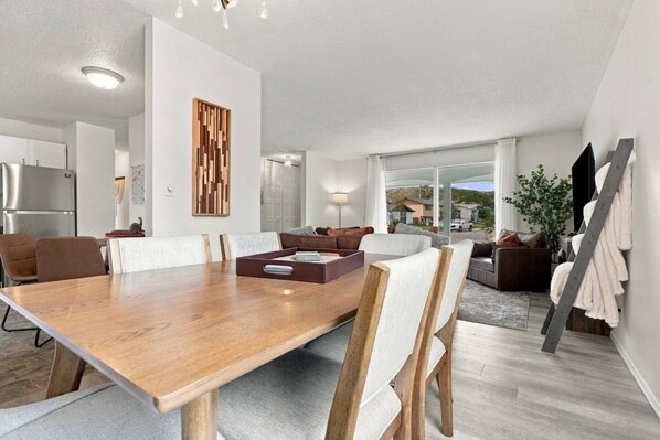 A modern living room with a wooden dining table, comfortable seating, and a large window offering a view.