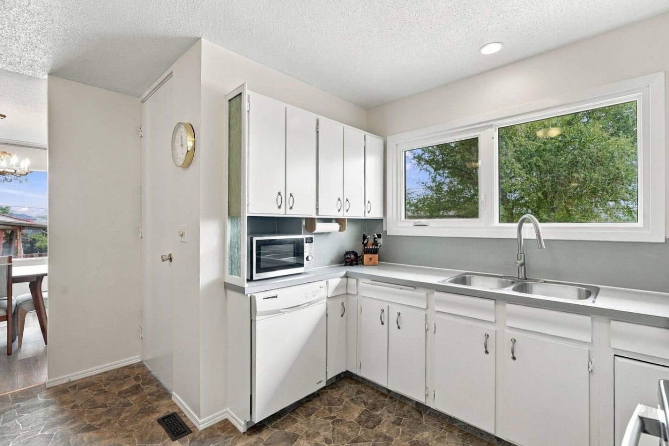 A modern kitchen with white cabinets, a built-in microwave, and a window overlooking greenery.