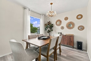 Un espace repas comprenant une table en bois, des chaises à revêtement gris, un lustre et des miroirs décoratifs fixés au mur.