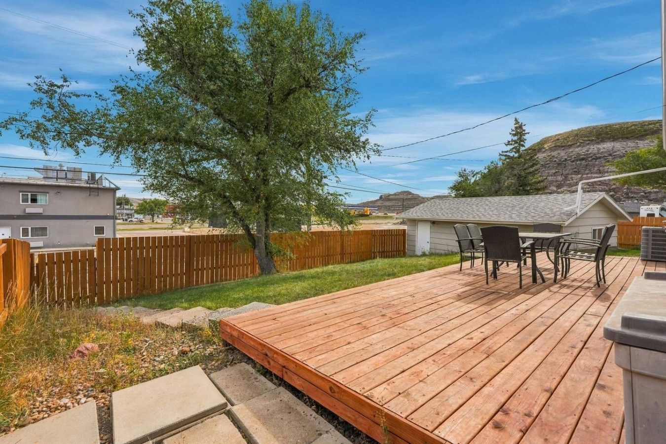 Une terrasse en bois avec des meubles d’extérieur, un arbre et une vue sur un quartier résidentiel.