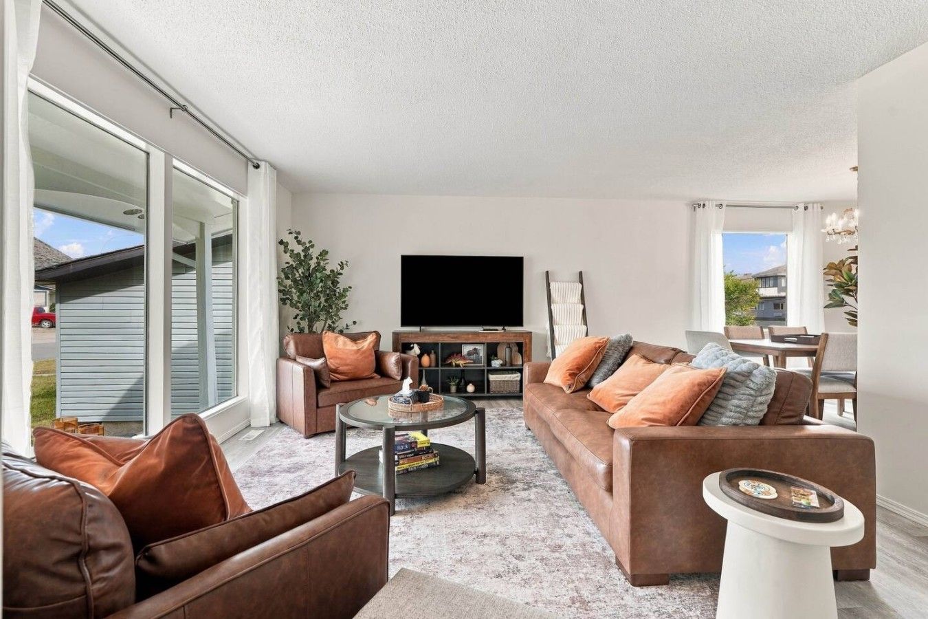 A living room with a sofa set, a coffee table, a flat-screen TV, and a dining area with chairs.