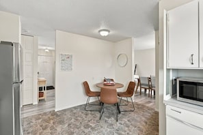 Une cuisine compacte avec un coin repas, des meubles blancs, un sol en pierre et un four à micro-ondes moderne.